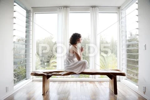 Woman Drinking Coffee On Bench In Sun Room
