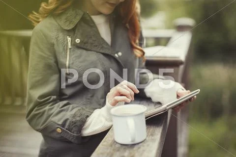 Woman drinking coffee using digital tablet at balcony railing Stock Photos