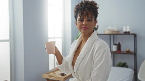 Woman drinking coffee while relaxing in a spa room, wearing a bathrobe, wit.. 스톡 동영상 286249715