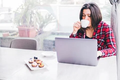 Woman drinking coffee while using laptop computer on table in cafe Foto stock