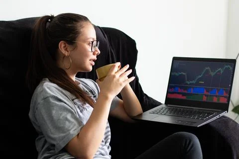Woman drinking coffee while viewing stock and investment charts on her laptop. Stock Photos