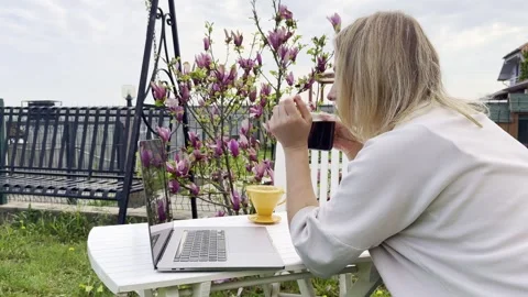 Woman Drinking Coffee While Working Remotely Outdoors in Spring 動画素材 334572181