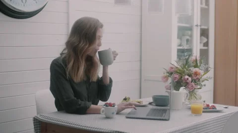 Woman drinking cup of coffee while typing on laptop in the kitchen Stock Footage 131044841