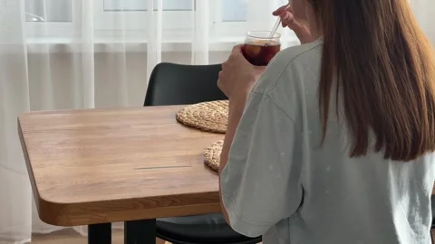 Woman drinking refreshing iced coffee through a straw at home at a table Stock Footage 340771085