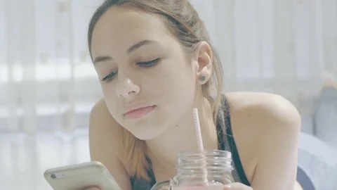 Woman is drinking a smoothies and using a fitness app on her smartphone. Stockbeeldmateriaal 73632665