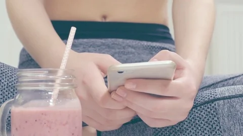Woman is drinking a smoothies and using a fitness app on her smartphone. Stock-Footage 73632829