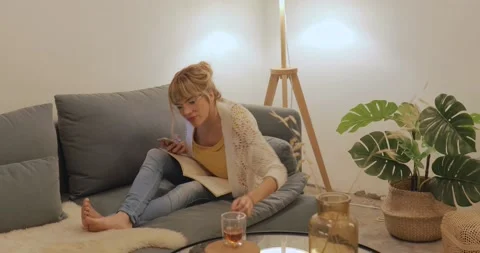Woman drinking tea and checking message smartphone from her couch Stock Footage 143799950