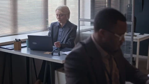 Woman Drinking Tea and Working on Laptop with Black Colleague in Office Stock Footage 334933261