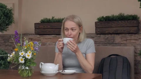 Woman drinking tea sitting at a table on the summer terrace cafe Stock Footage 132937293