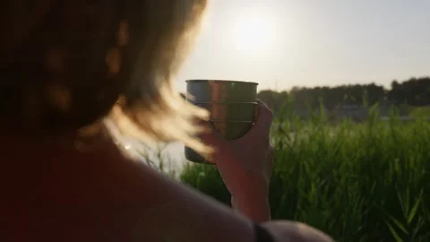 Woman Drinking Warm Tea from Thermo Cup Near Calm Lake at Sunset Stock Footage 344769858
