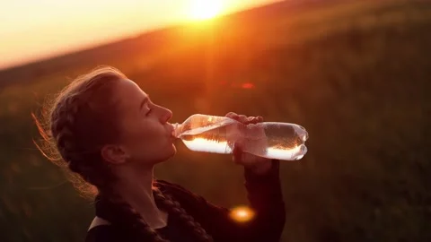 Woman drinking water from a bottle while walking, standing in a field Stock Footage 236208211