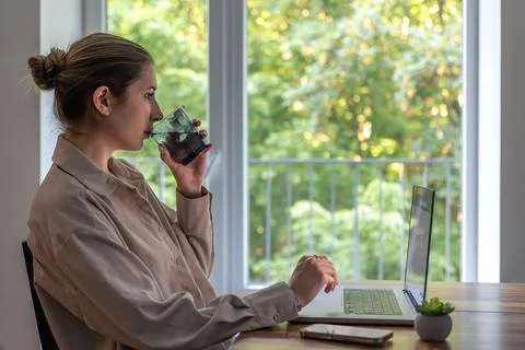 Woman drinking water while using laptop. Remote work at home. 스톡 사진