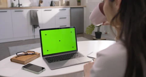 Woman drinks coffee while looking at laptop screen at dining table in kitchen Stock Footage 237929867