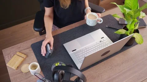 Woman drinks coffee while using laptop and computer mouse Stockbeeldmateriaal 346729512