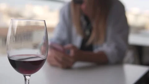 A woman drinks red wine at a table while using her phone Stock Footage 307997458