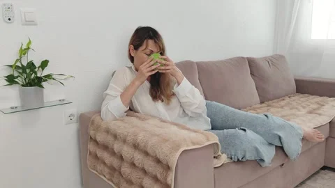 Woman drinks tea while sitting on the sofa in a large bright living room. Stock Footage 276920059