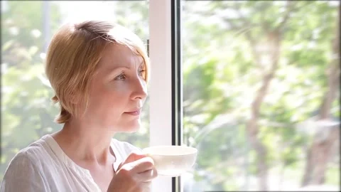 A woman drinks tea at the window closing her eyes with pleasure Stock Footage 156365486