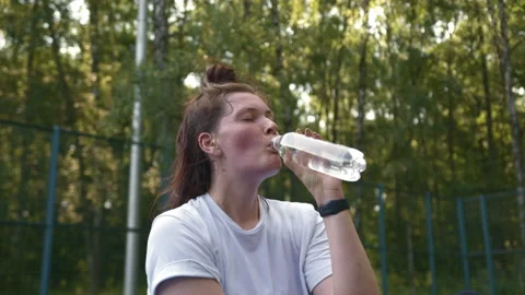 Woman drinks water from a bottle while sitting on sports platform after training Stock Footage 157105704