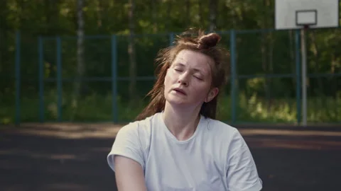 Woman drinks water from a bottle while sitting on sports platform after training Stock Footage 157113445