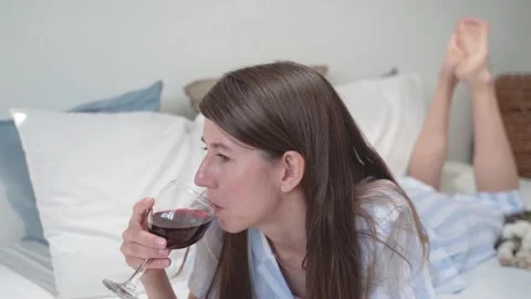 A woman drinks wine while lying in bed. A woman holds a glass of wine. Relax at Stock Footage 155804715