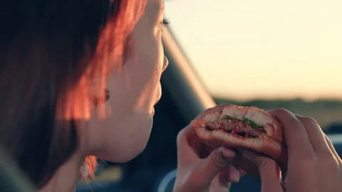 Woman driver eats fresh burger resting in car at sunset countryside closeup Stock Footage 252550101
