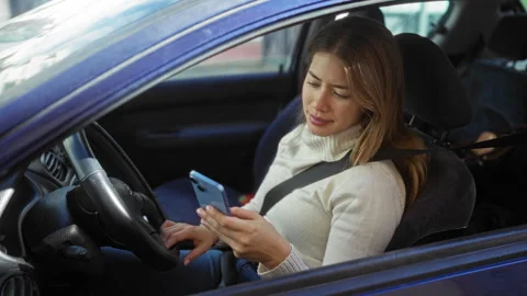 Woman driving car while using phone on urban street with sunlight reflectin.. Stock Footage 310040903