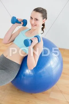 Woman with dumbbells on exercise ball in fitness studio Stock Photos