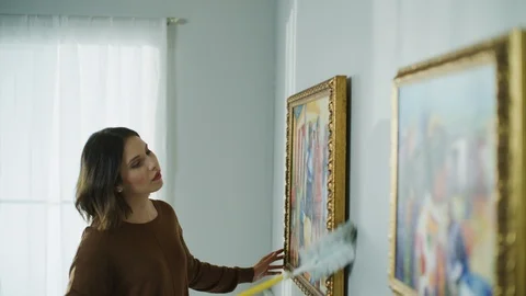 Woman dusting frames of paintings on wall / Cedar Hills, Utah, United States Stock Footage 106943712