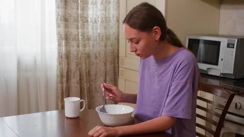 Woman eating breakfast cereal at kitchen table morning routine Stock Footage 342556053