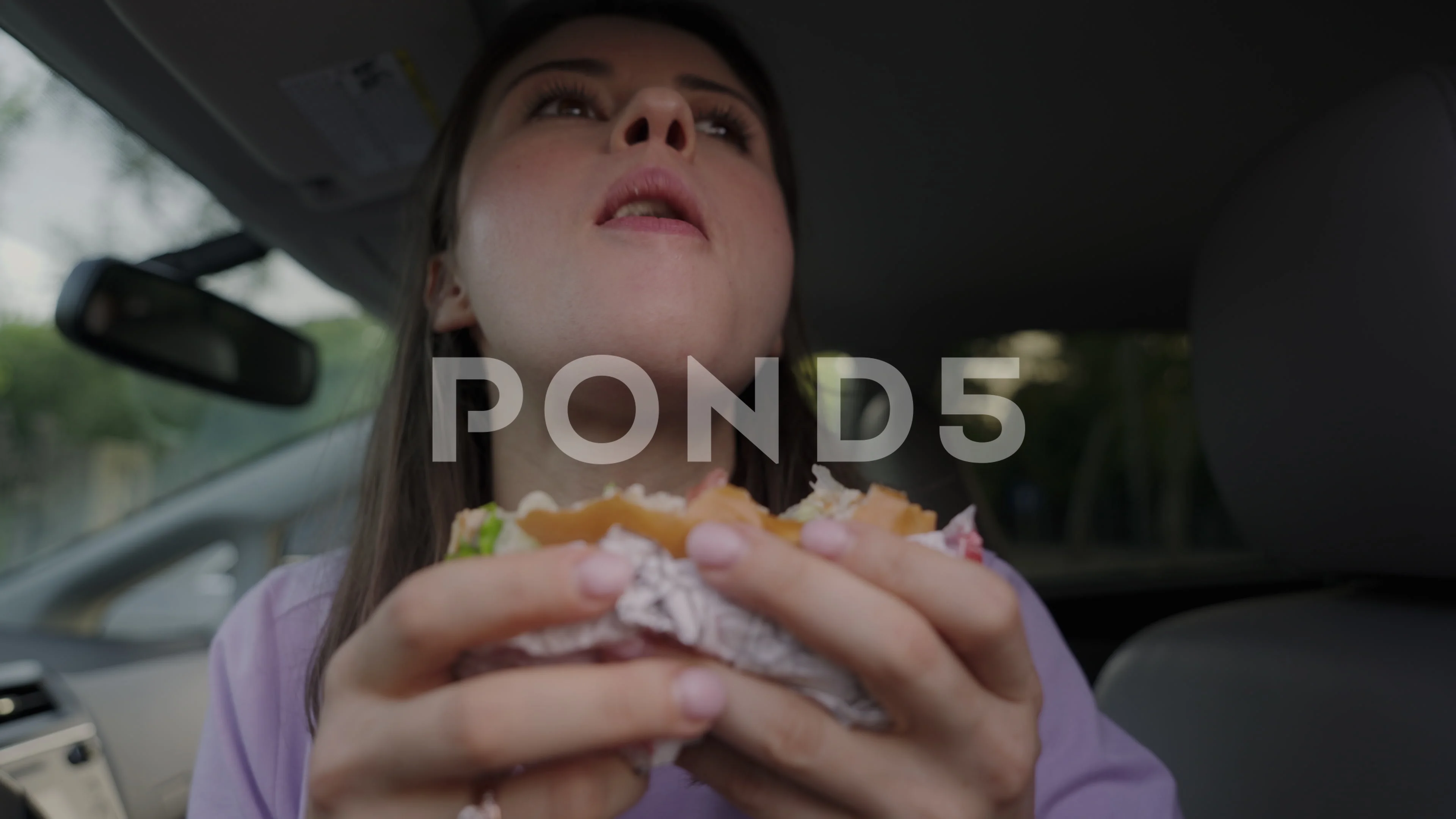 Woman eating burger in the front seat of the car during the morning  journey. Car