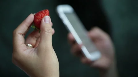 Woman eating a strawberry while using mobile device. Stock Footage 64050625
