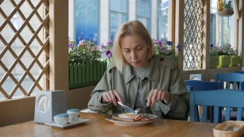 A woman eats Breakfast in a cafe, with a knife cuts the sausage in the dish Stock Footage 131608707