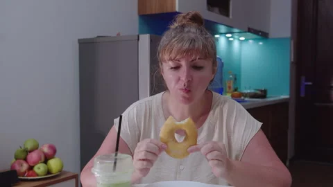 A woman eats a curd ring, sitting at a table, against the background of the Stock Footage 329938947