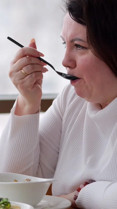 Woman eats dessert with spoon at table, looking focused as she lifts bite and 動画素材 346407276