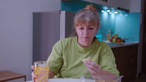 Woman eats a fresh pie with an appetite and washes it down with juice, sitting Stock Footage 329937451