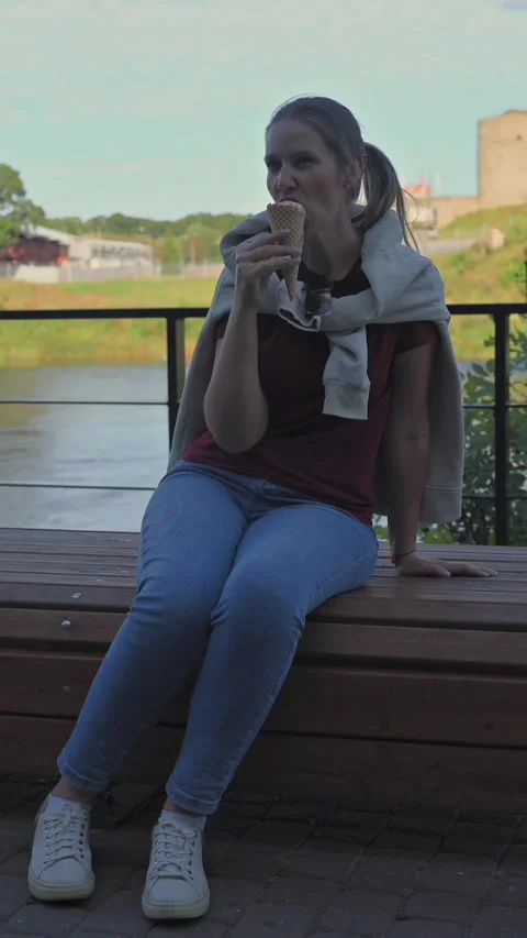 Woman eats ice cream sits on bench by river near castle at sunset. Vertical Stock Footage 342341087