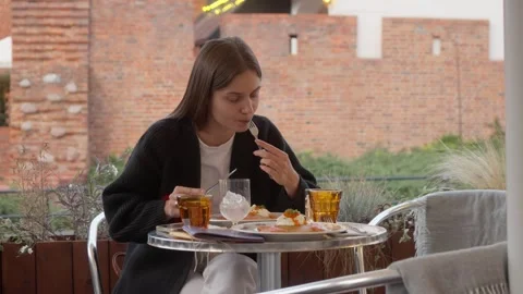 A woman eats lunch at a table on the summer terrace of a city restaurant or cafe Stock Footage 307695076