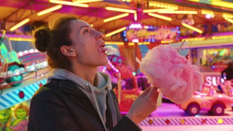 Woman eats pink cotton candy at a festive children's event against the backdrop Stock Footage 237523652