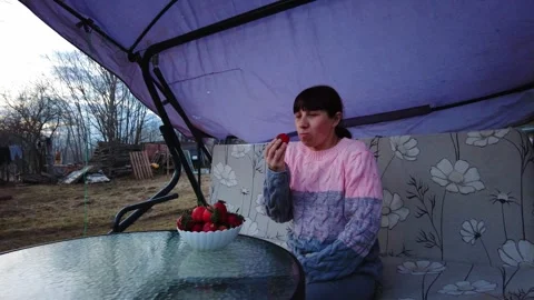 Woman eats strawberries while sitting outside under a canopy in a garden during Stock-Footage 332066857