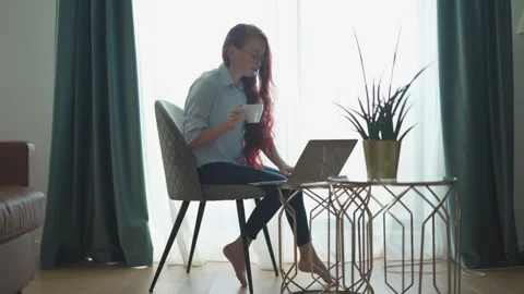 A woman engaged in her work while comfortably seated at home, utilizing her 스톡 동영상 289965893