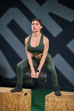 Woman engages in squat exercise while holding dumbbells in fitness setting. She Stock Photos