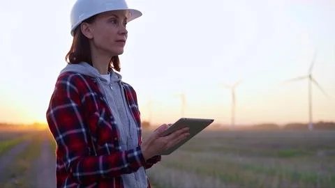 Woman engineer taking notes with a tablet computer on a field with wind turbines Foto stock