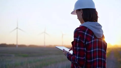 Woman engineer taking notes with a tablet computer on a field with wind turbines Foto stock