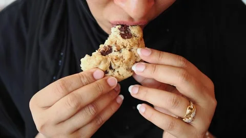 Woman enjoying a cookie while taking a bite in a casual setting Stock Footage 346665528