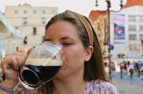 A woman is enjoying a dark beer while sitting outside in a lively urban setting. Stock Photos