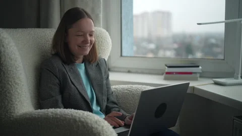 Woman enjoying her work while smiling at her laptop in a cozy apartment with Stock Footage 322164958