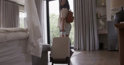 Woman is entering frame while pulling wheeled suitcase toward sliding door to Stock Footage 335928142