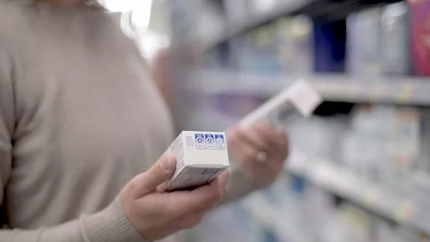 A woman examines two boxes of toothpaste in a store aisle, comparing them. Th Stock Footage 276719622