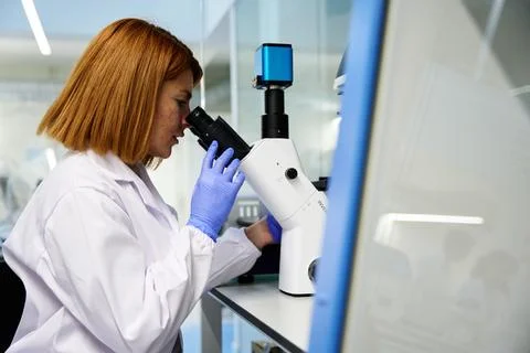 Woman examining a sample through a microscope in a modern laboratory Фото