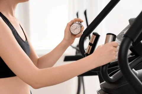 Woman exercising on an elliptical machine while holding a stopwatch for fitne Stock Photos